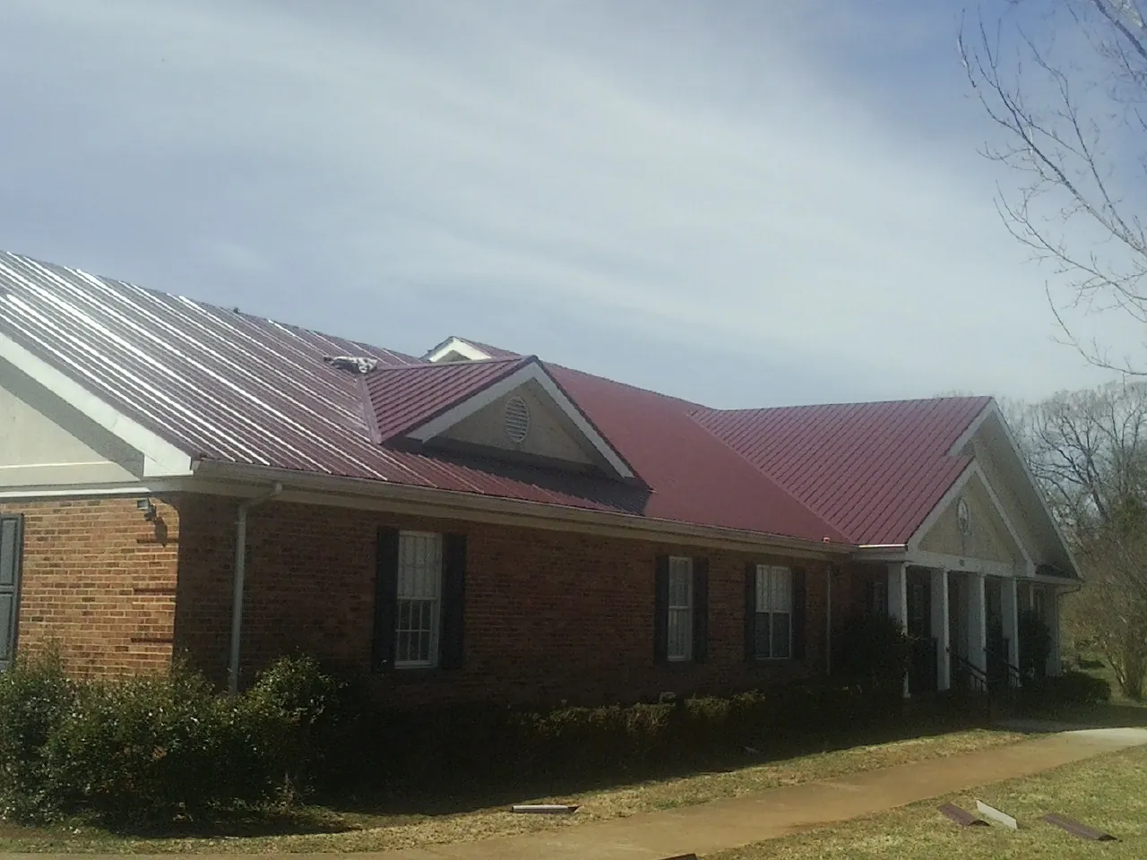 Red metal roof with gabled entries on a long brick building, from a Hail Damage Roof Repair job in Adrian