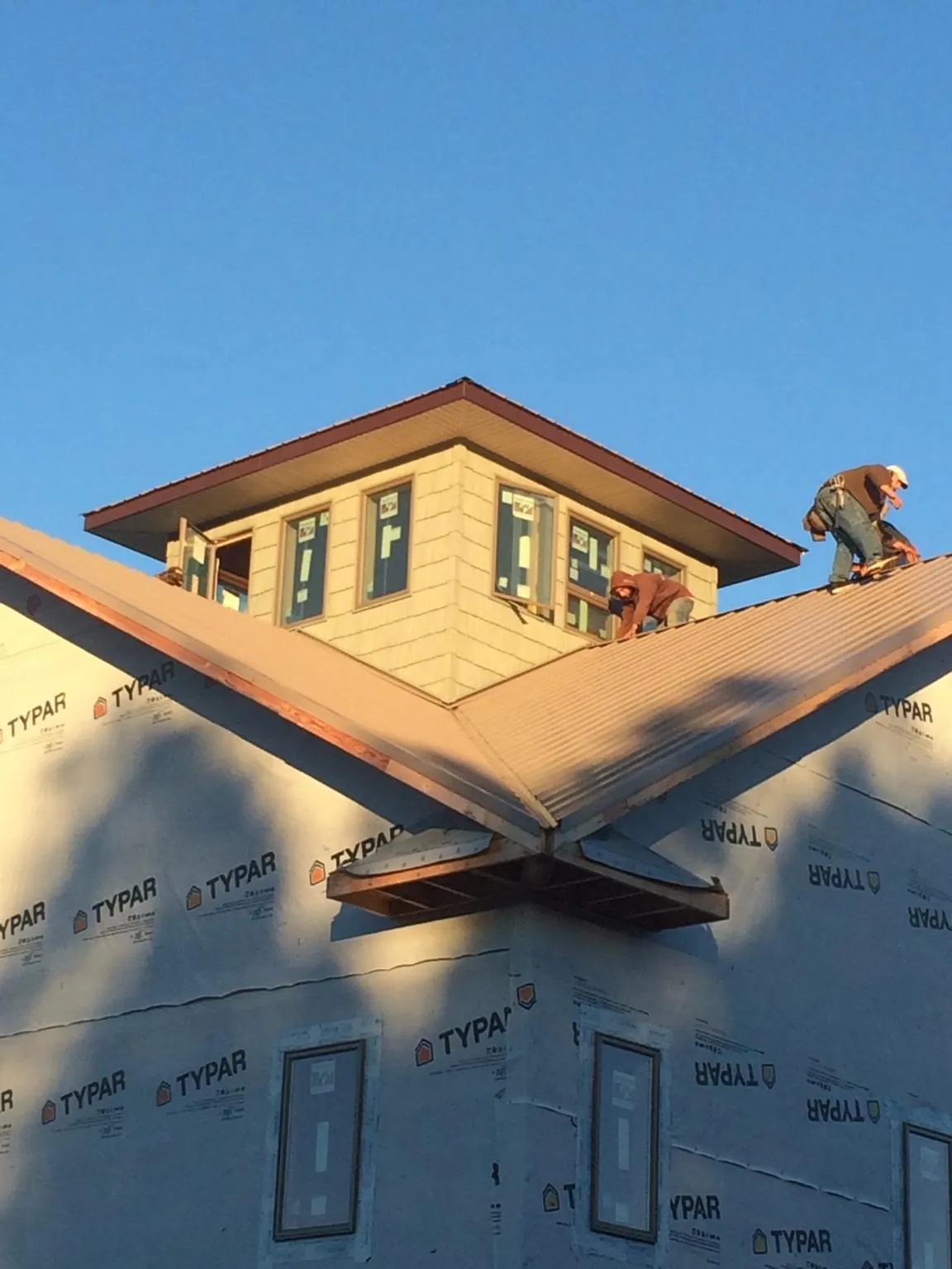 Roofers working around a rooftop cupola on a new metal roof at sunset — Roof Waterproofing in Adrian by Roofing Brothers